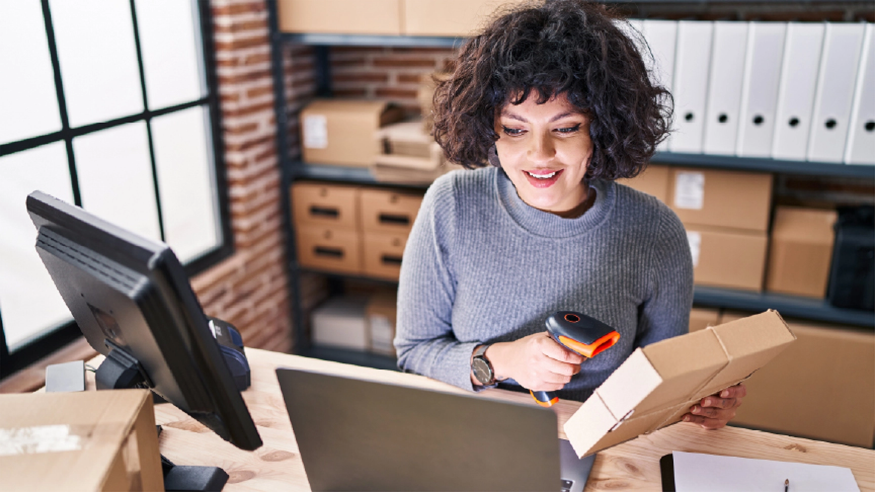 Woman looking at screen and holding box to ship out from store