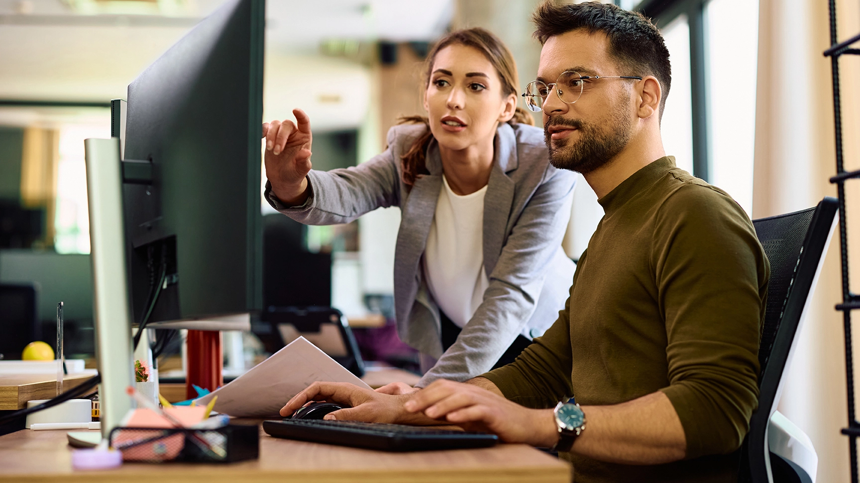 A man at a computer, with a woman next to him pointing at the screen