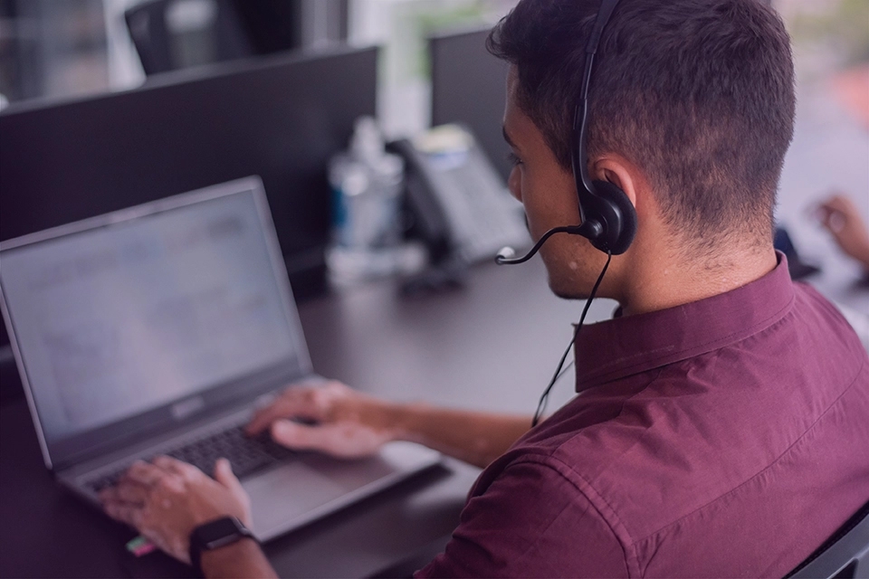 An over the shoulder view of a call center employee at his work station wearing a headset