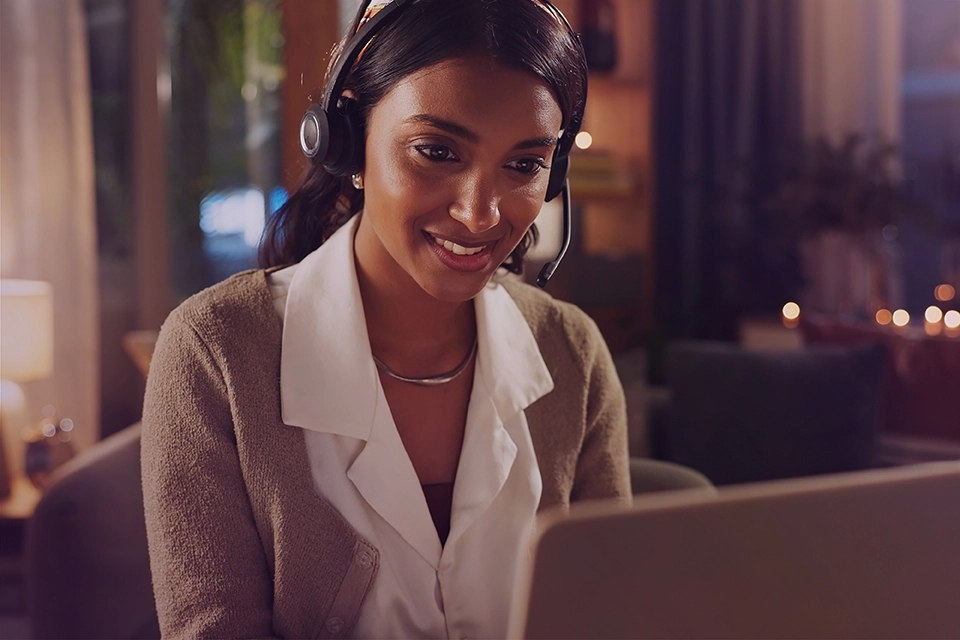 A woman working on a laptop wearing a headset